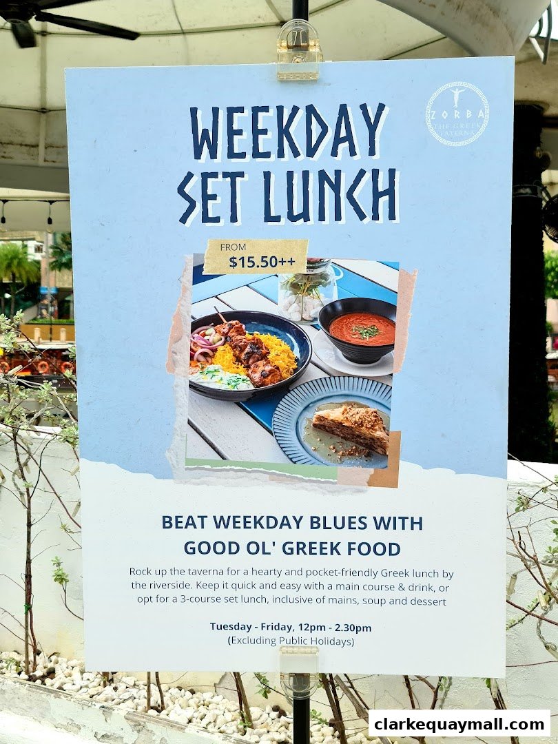 A sign advertising Zorba The Greek Taverna's weekday set lunch with images of Greek food.