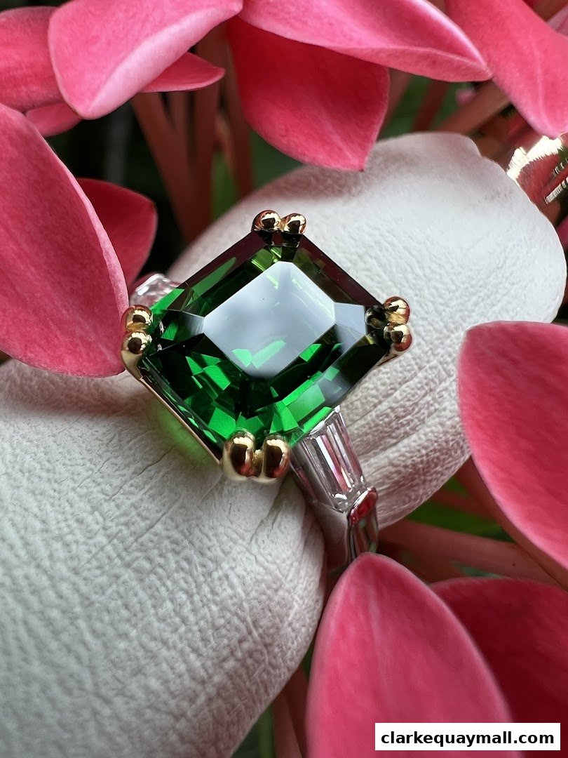 A close-up of a stunning emerald ring with gold accents, surrounded by pink petals.