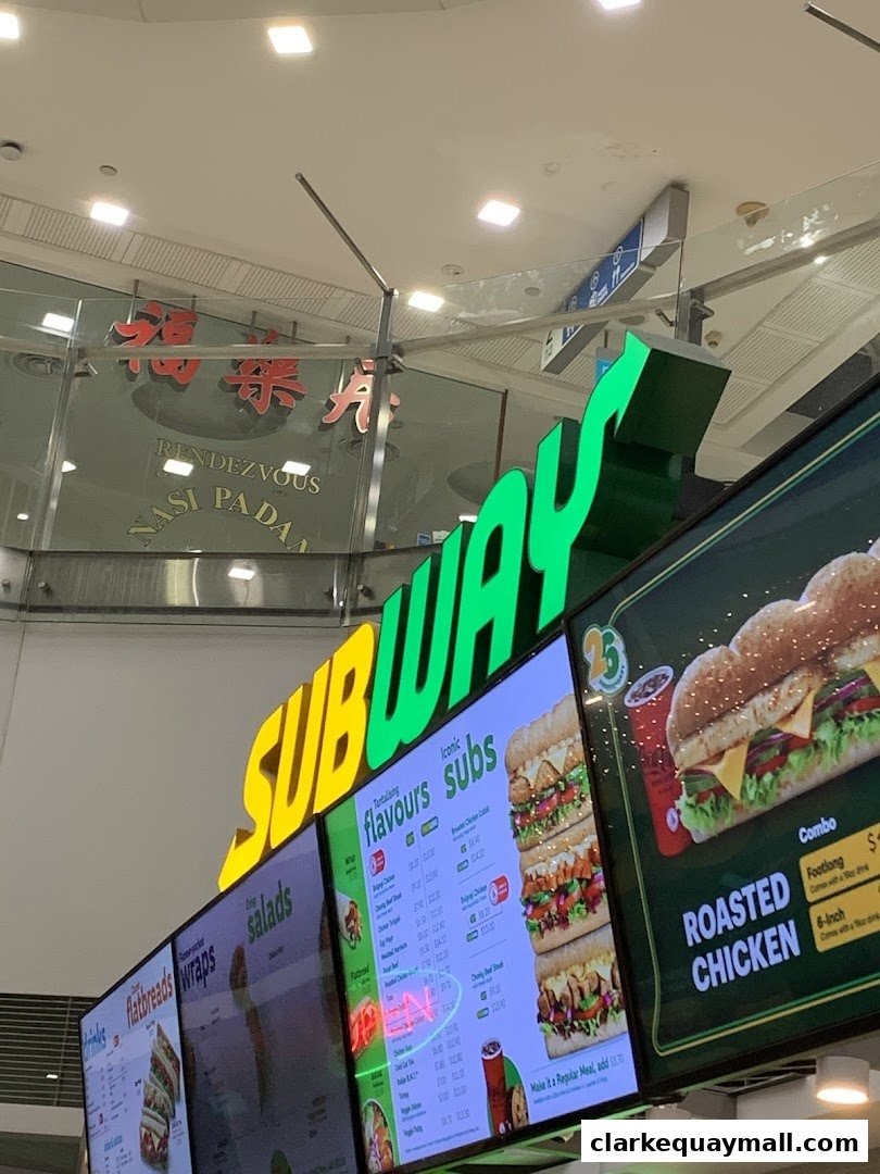 A Subway restaurant sign and digital menu boards displaying various sandwich options.
