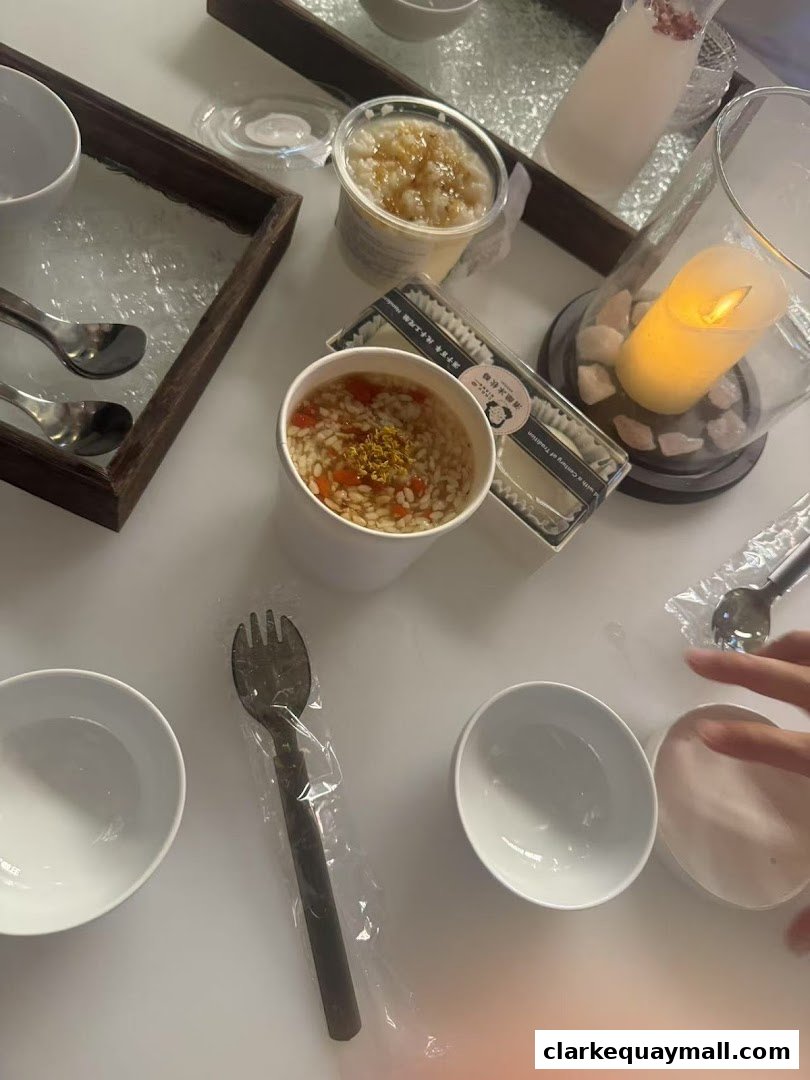 A table setting with bowls, spoons, a fork, and two desserts, one in a cup and another in a container.