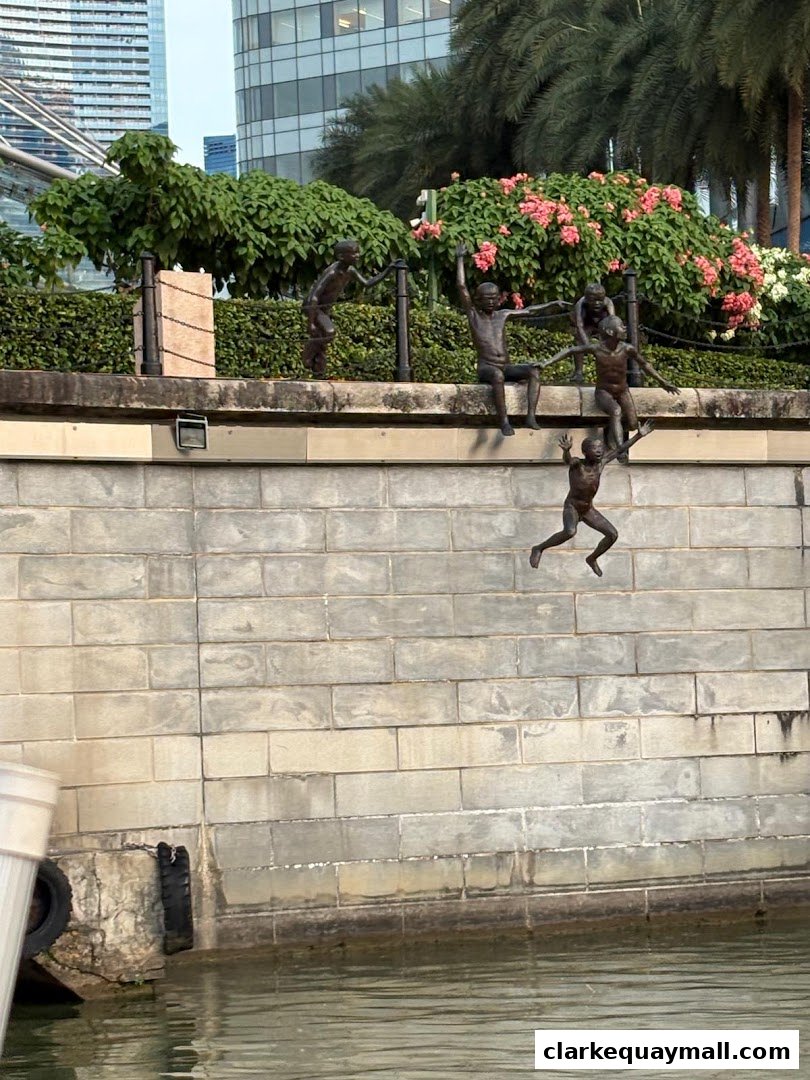 Bronze sculptures of children jumping into the Singapore River with lush greenery and buildings in the background.