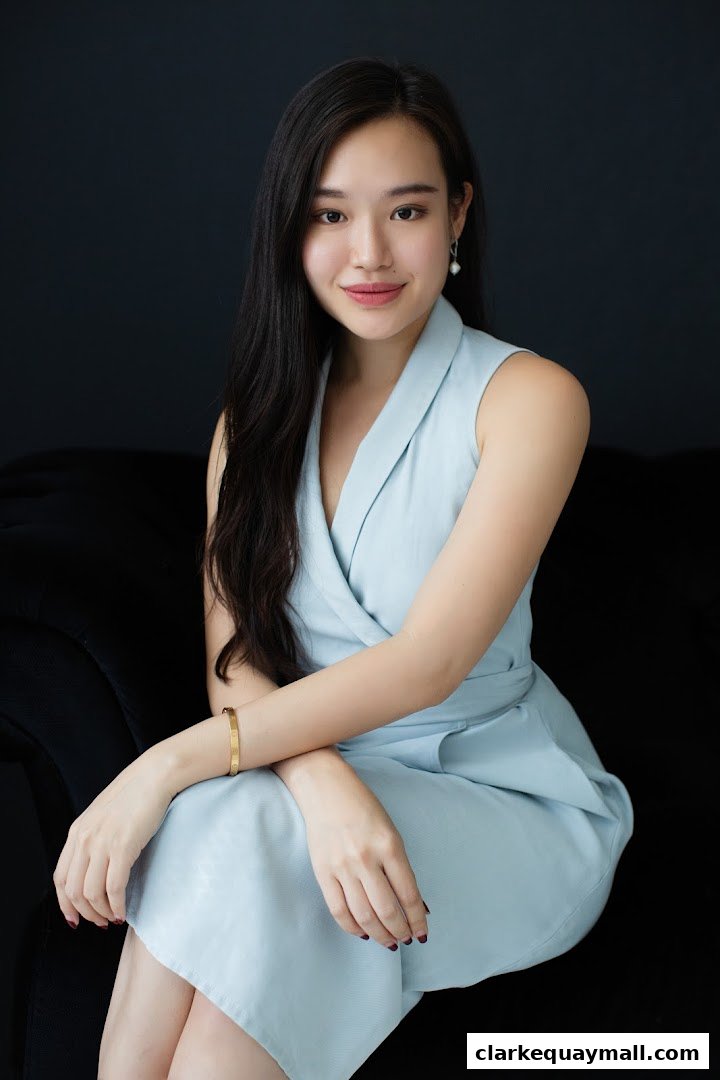 A professional portrait of a young woman in a light blue dress against a dark background.