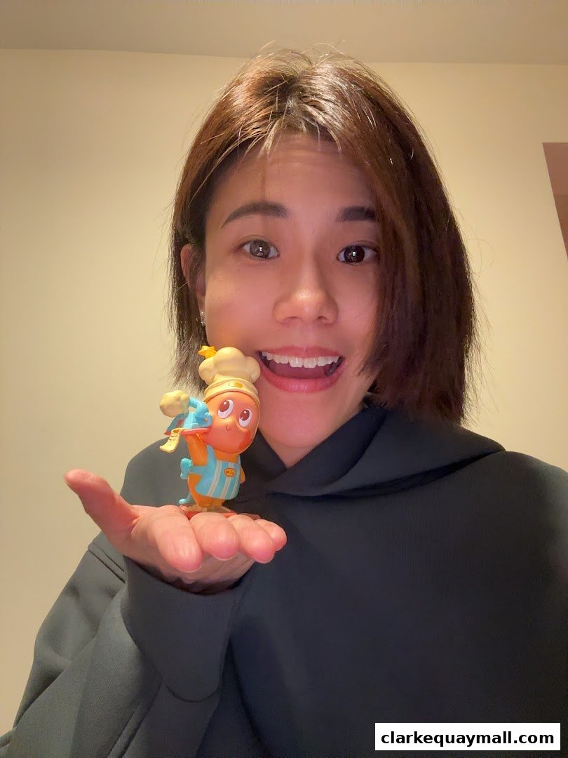 A woman smiles while holding a small, cartoonish figurine on her palm.