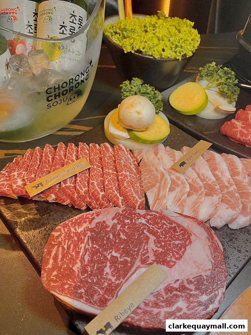 A selection of premium Korean BBQ meats, including Ribeye and Boneless Short Ribs, with Soju bottles and fresh greens.
