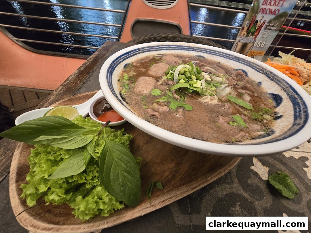 A steaming bowl of pho with beef, herbs, and a side of fresh vegetables and lime.
