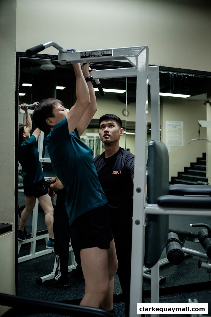 A trainer supervises a client performing pull-ups in a gym.