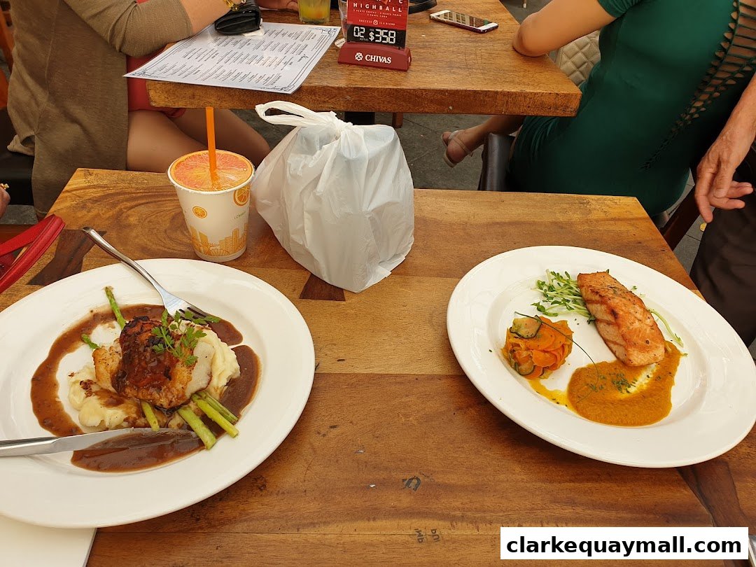 Two plates of food and drinks are on a wooden table with people dining.