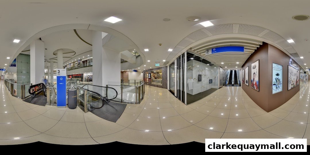 A panoramic view of a shopping mall corridor with escalators and various shop fronts.
