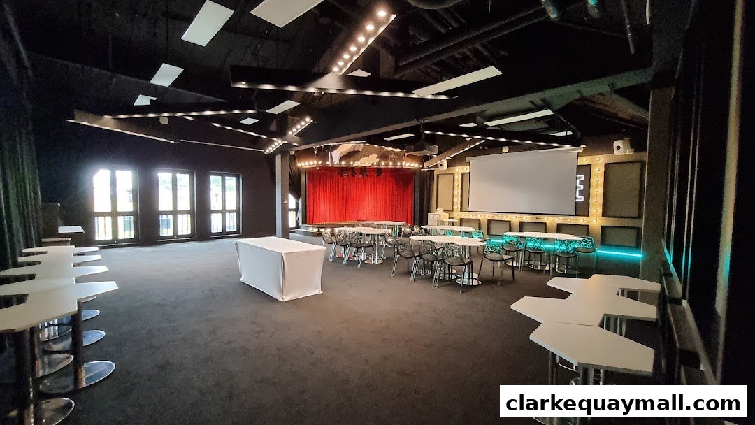Interior of a modern event space with a stage, seating, and a projector screen.