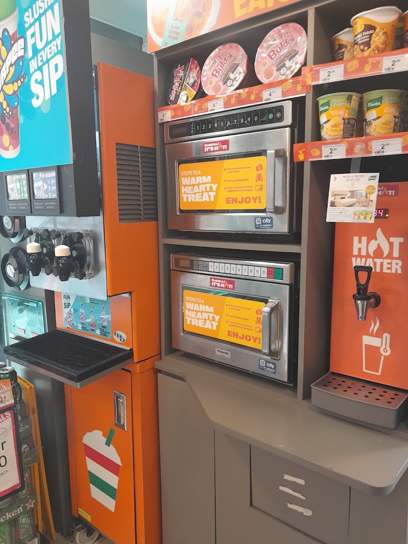 Interior view of a 7-Eleven convenience store featuring self-service Slurpee, microwave stations, and hot water dispenser.