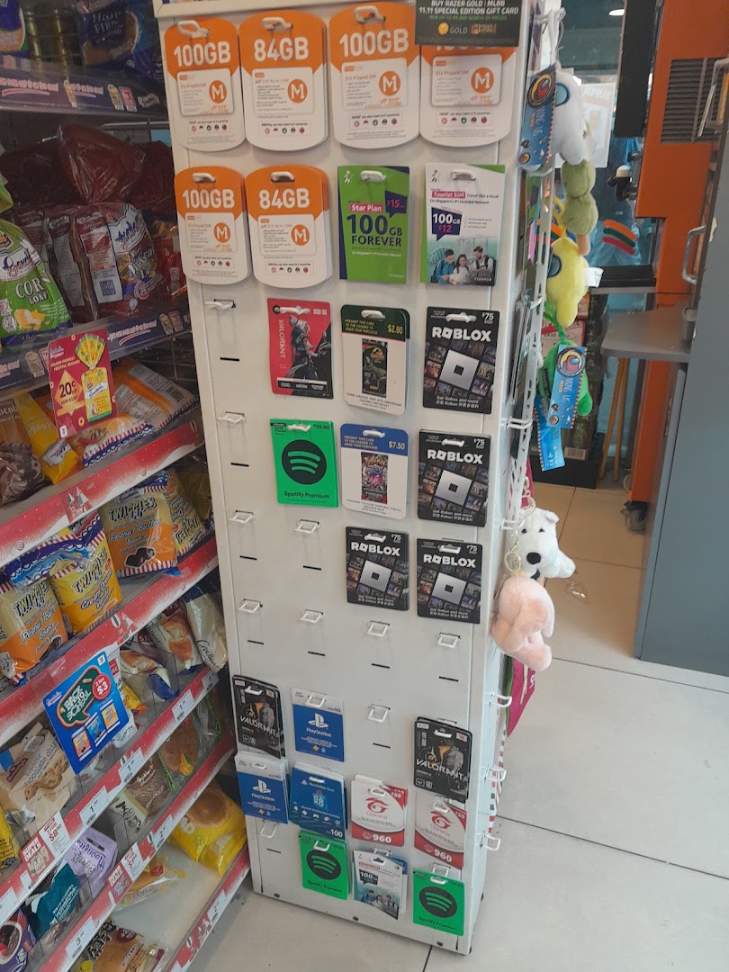 A display rack inside 7-Eleven featuring various gift cards, SIM cards, and digital vouchers next to snack shelves.