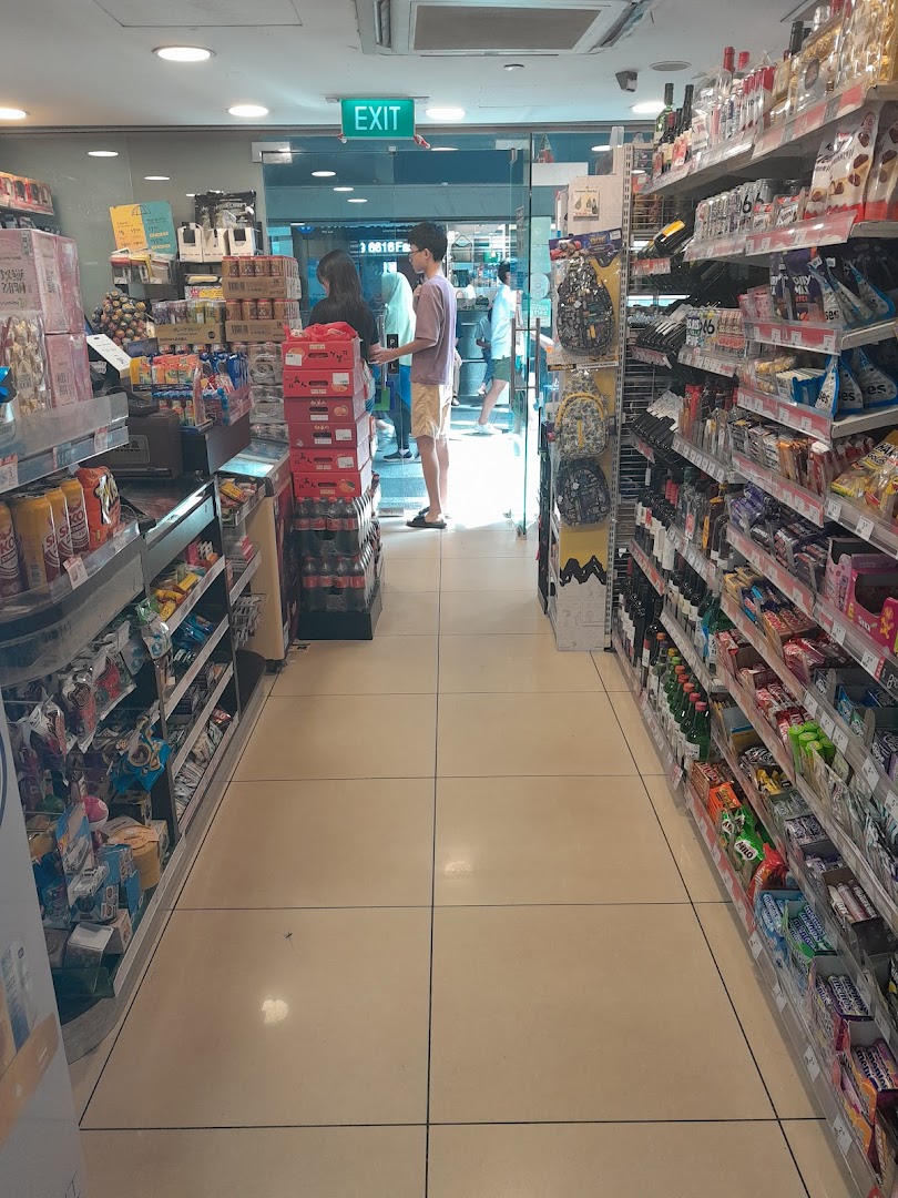An interior view of a 7-Eleven store aisle, showcasing shelves stocked with various products and customers near the exit.
