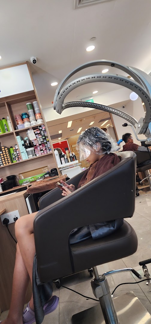 A customer relaxing under a hair treatment machine with a face shield, using a phone in a hair salon.