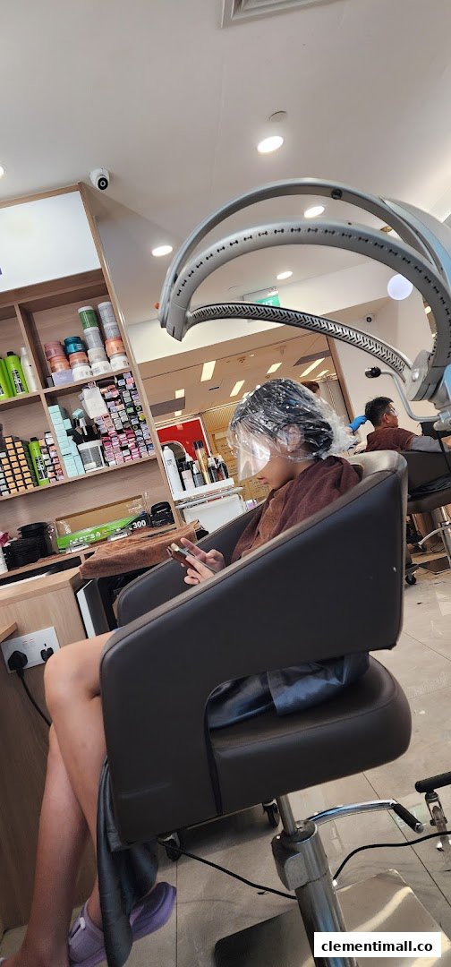 A customer relaxing under a hair treatment machine with a face shield, using a phone in a hair salon.
