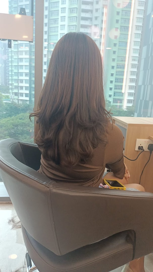 A customer with freshly styled brown hair sits in a salon chair, facing a large window with a city view.
