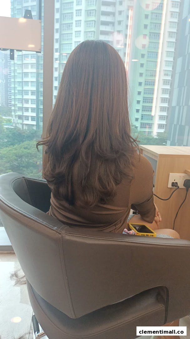 A customer with freshly styled brown hair sits in a salon chair, facing a large window with a city view.