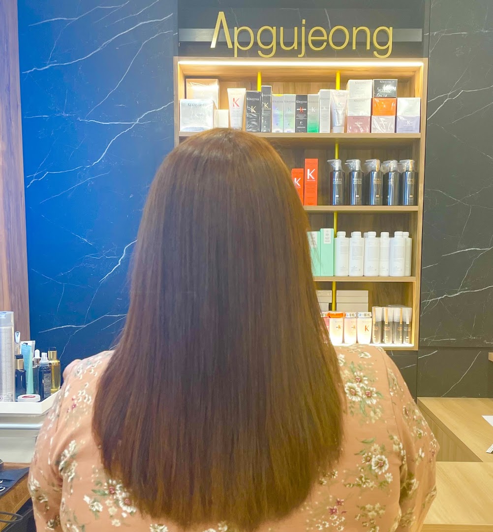 A customer with long brown hair sits in a salon, facing shelves of hair products.