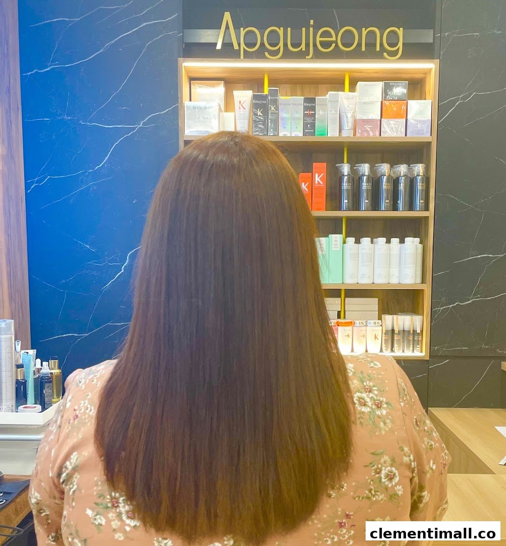 A customer with long brown hair sits in a salon, facing shelves of hair products.
