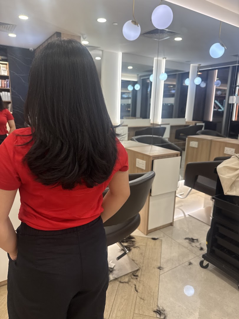 A customer with long dark hair from behind, in a modern hair studio with cut hair on the floor.