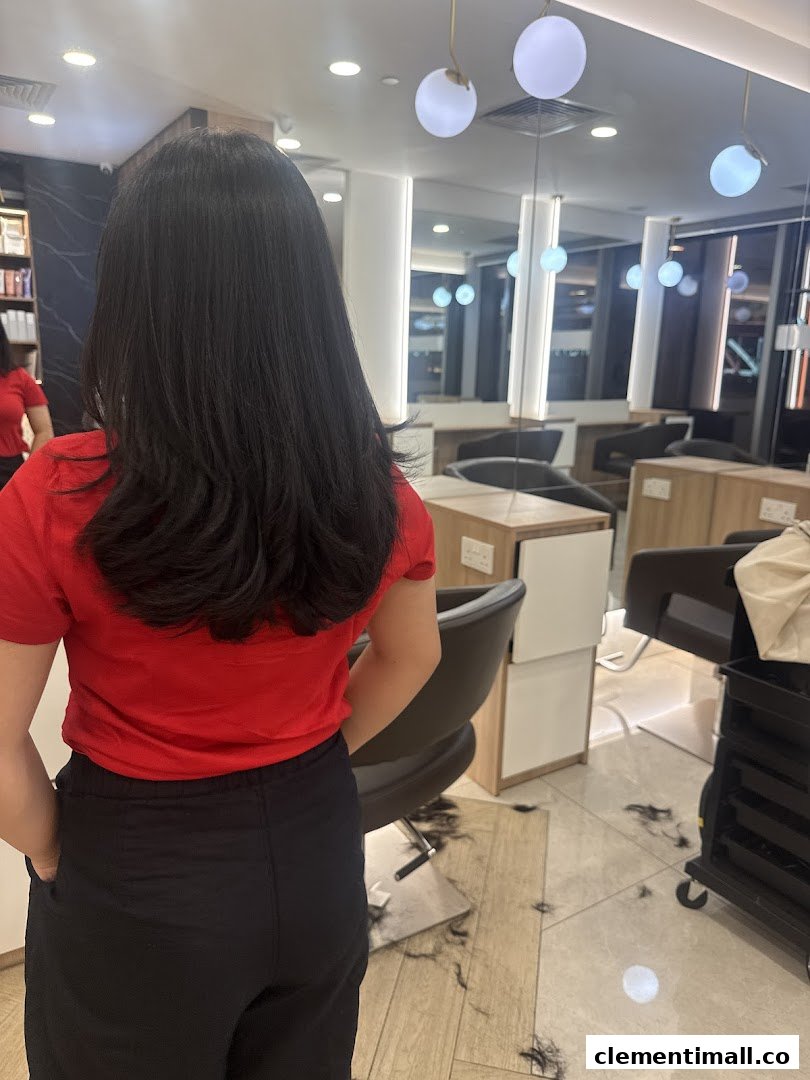 A customer with long dark hair from behind, in a modern hair studio with cut hair on the floor.