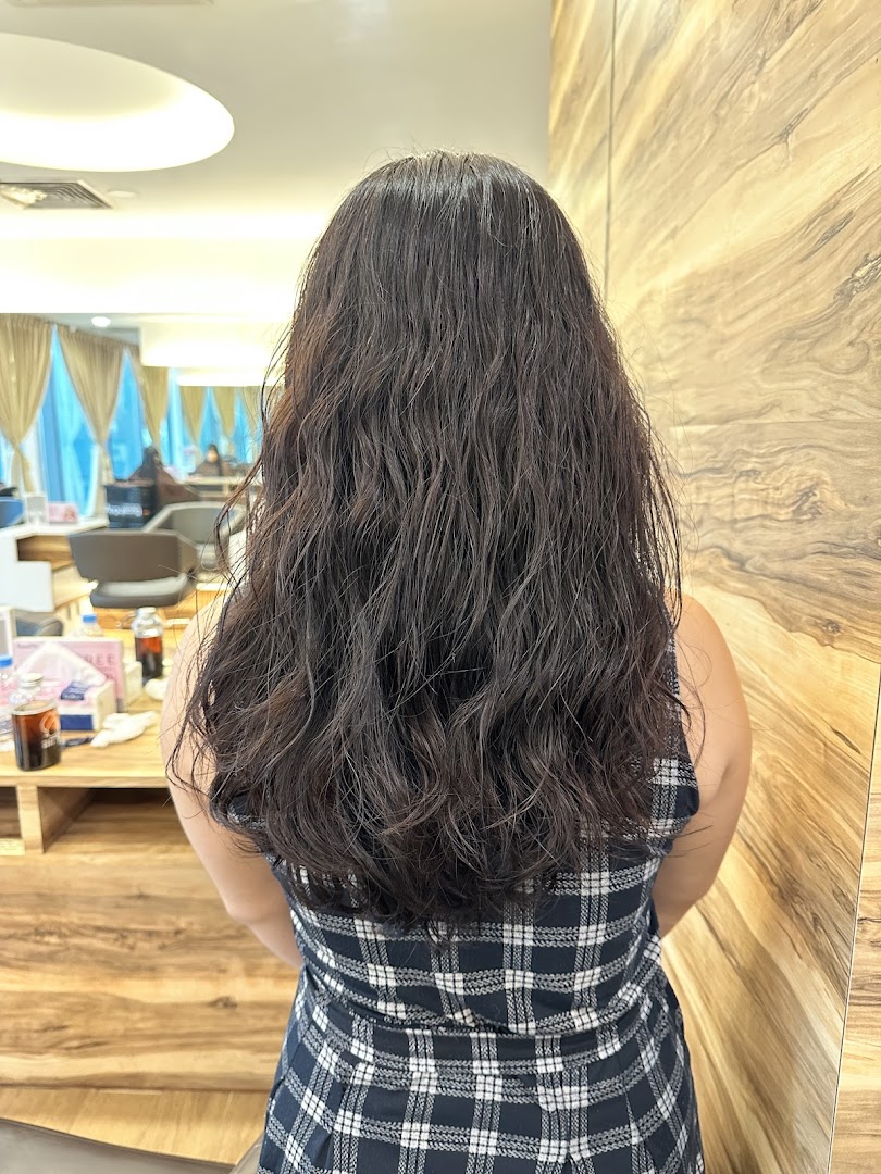 A person with long, wavy dark hair from behind, inside a modern hair salon.