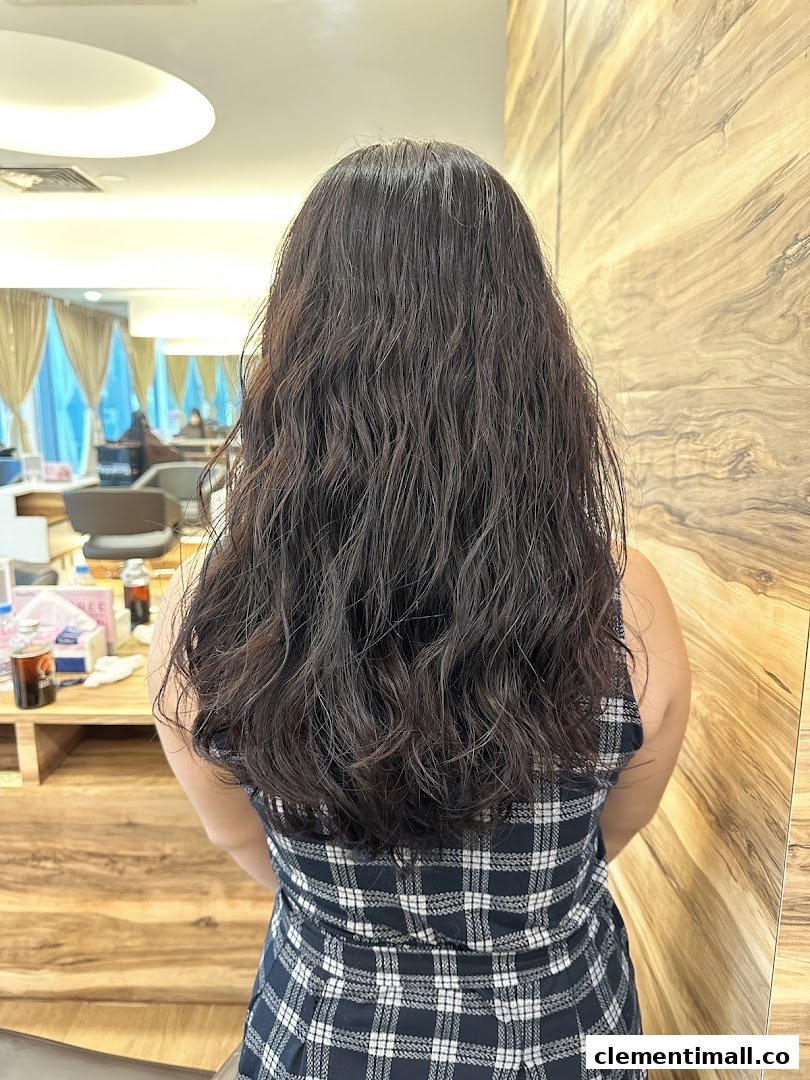 A person with long, wavy dark hair from behind, inside a modern hair salon.