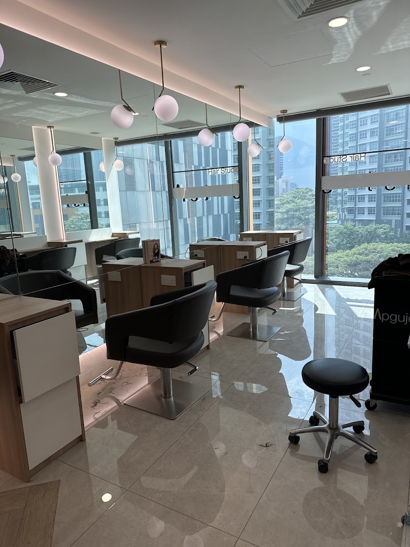 A bright, modern hair studio interior with multiple styling stations and large windows overlooking city buildings.
