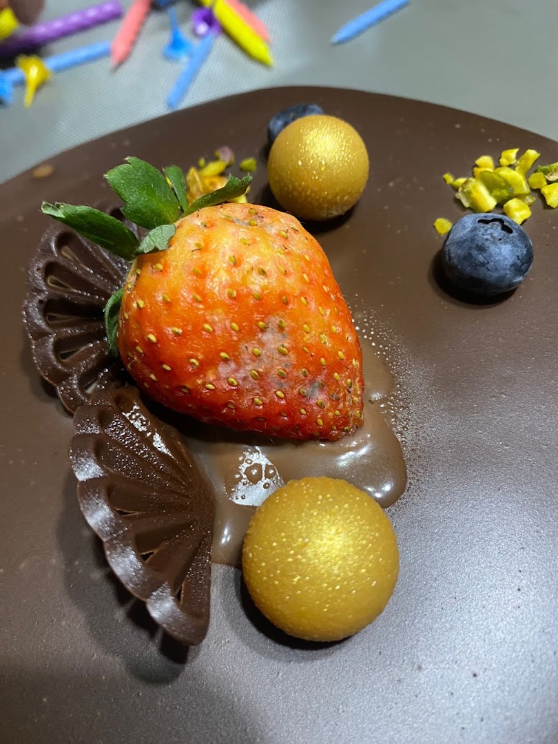 Close-up of a chocolate cake decorated with a fresh strawberry, blueberries, and golden spheres.