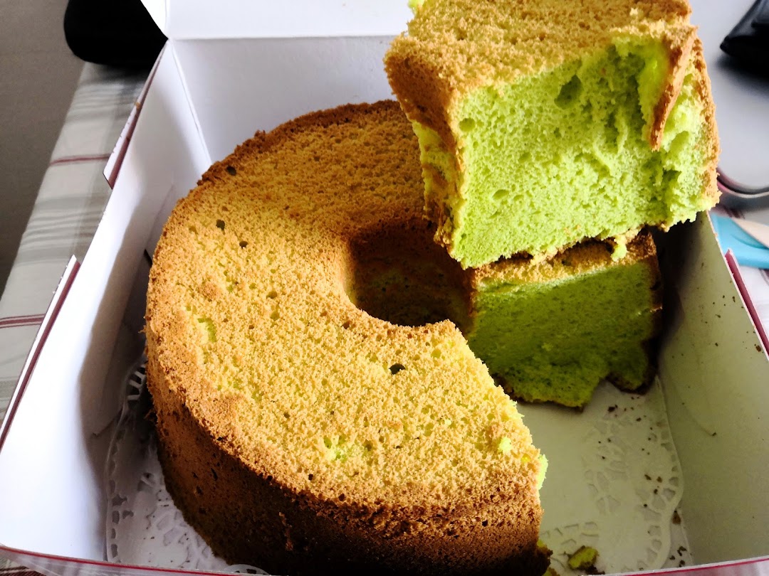 A vibrant green pandan chiffon cake, partially cut, presented in a white bakery box.