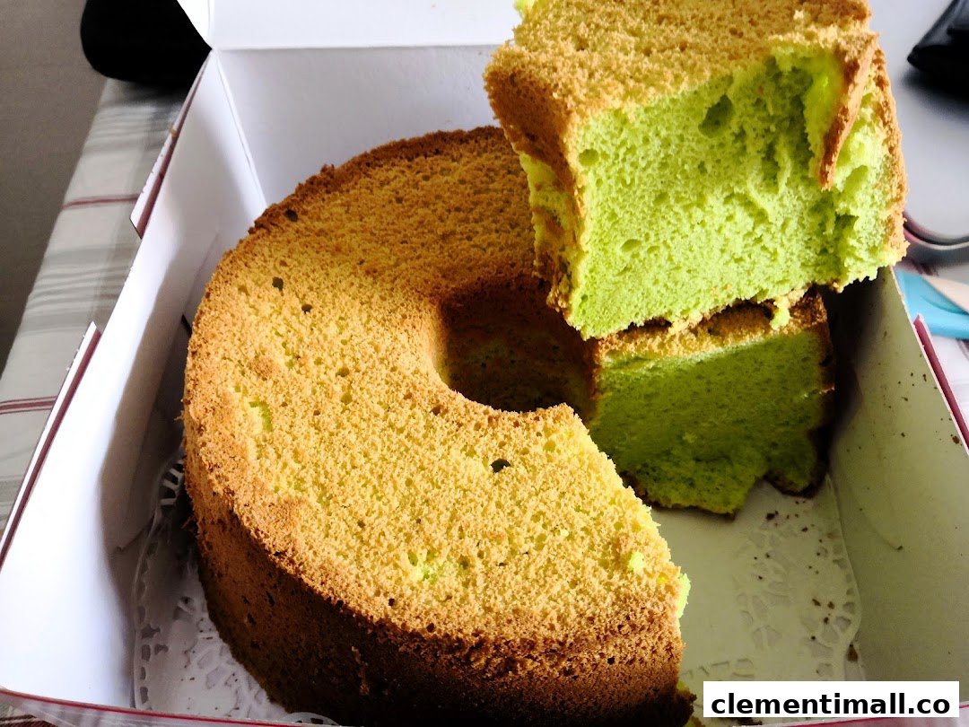 A vibrant green pandan chiffon cake, partially cut, presented in a white bakery box.