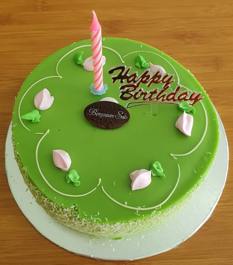 A vibrant green birthday cake from Bengawan Solo with a candle and 'Happy Birthday' topper.