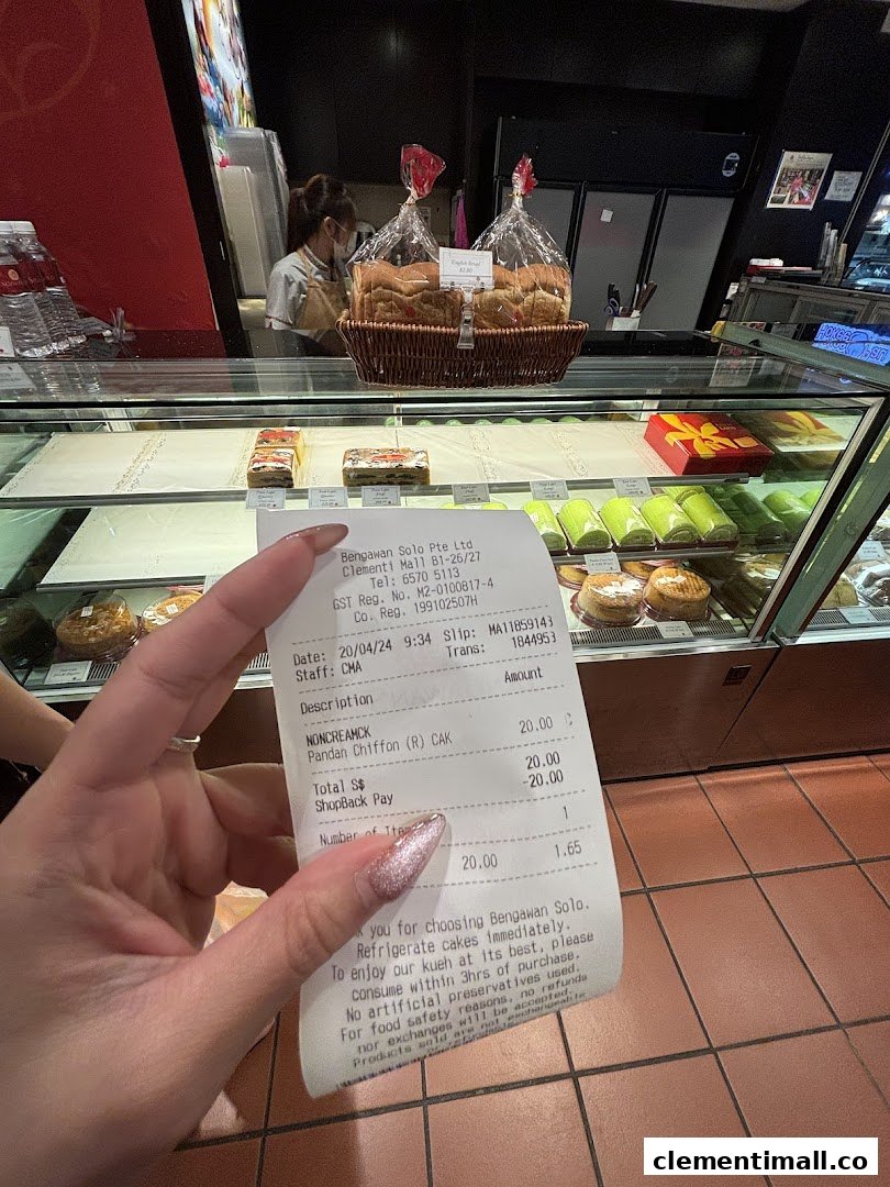 A hand holds a receipt in front of a display case filled with cakes and pastries at Bengawan Solo.