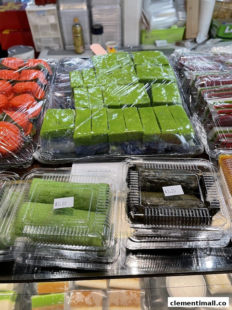 Assorted traditional Indonesian kueh and snacks, including green pandan cakes, displayed in clear packaging.