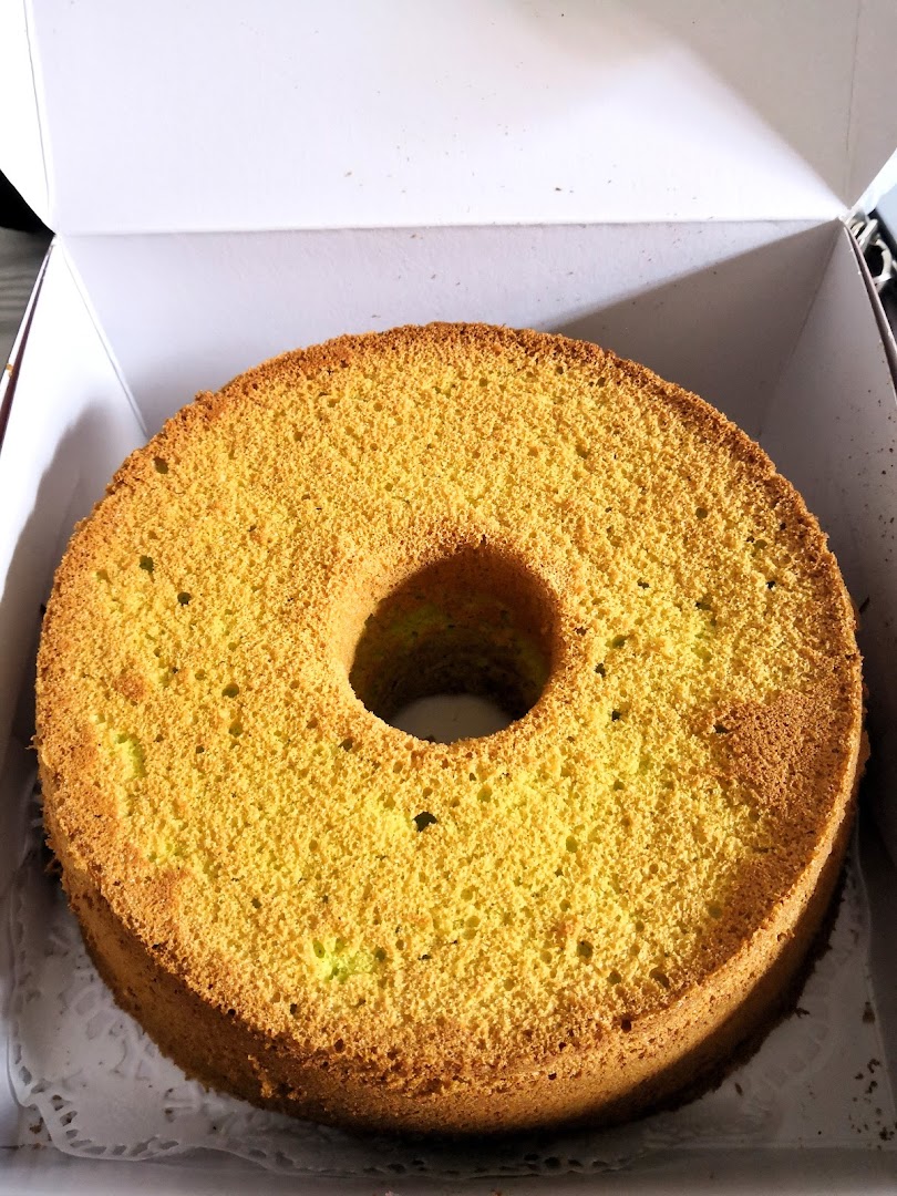 A golden-brown chiffon cake with a hole in the center, presented in a white bakery box.