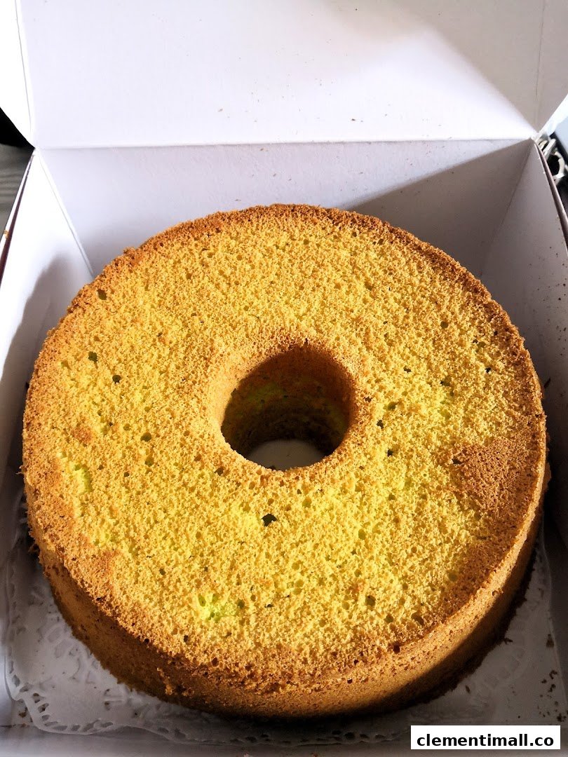 A golden-brown chiffon cake with a hole in the center, presented in a white bakery box.