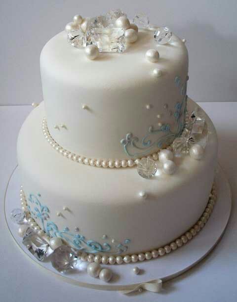 A beautifully decorated two-tier white cake adorned with pearls, clear gems, and delicate blue icing.