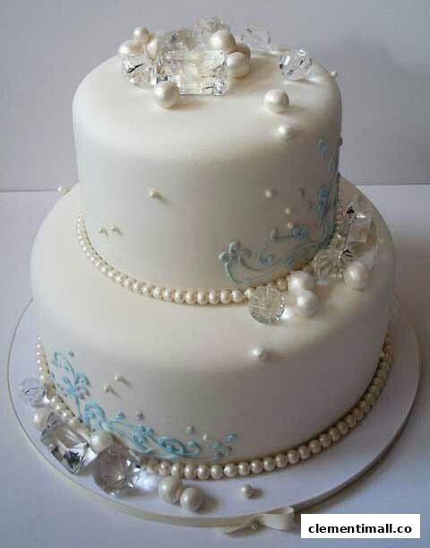 A beautifully decorated two-tier white cake adorned with pearls, clear gems, and delicate blue icing.
