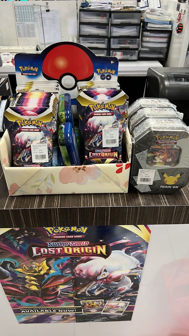 A display of Pokémon Trading Card Game products, including booster packs and tins, on a counter.