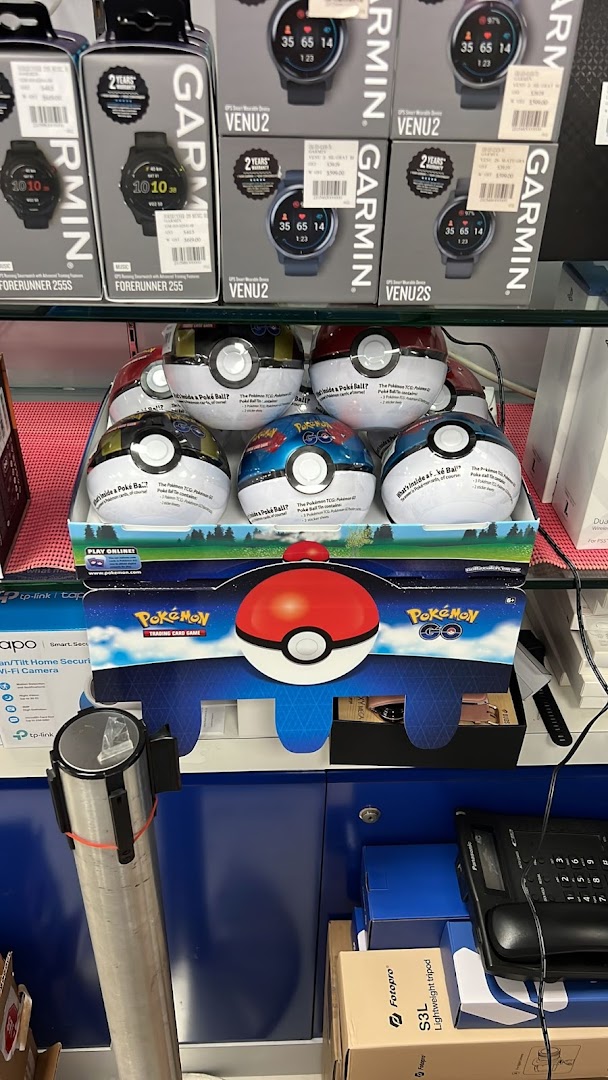 A retail display featuring Garmin smartwatches and Pokémon Trading Card Game Poke Ball products inside an electronics store.
