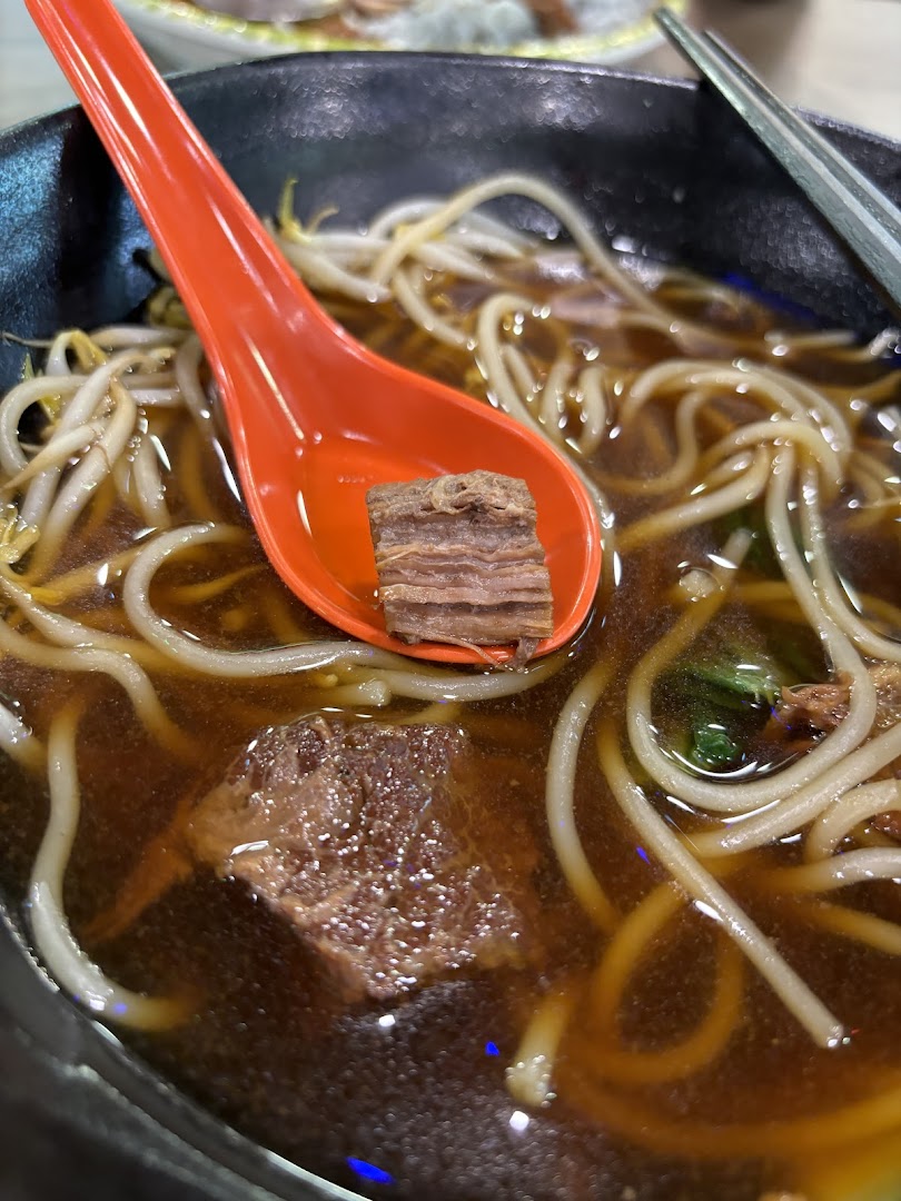 A close-up of a hearty bowl of beef noodles with bean sprouts, featuring a tender beef chunk on a spoon.