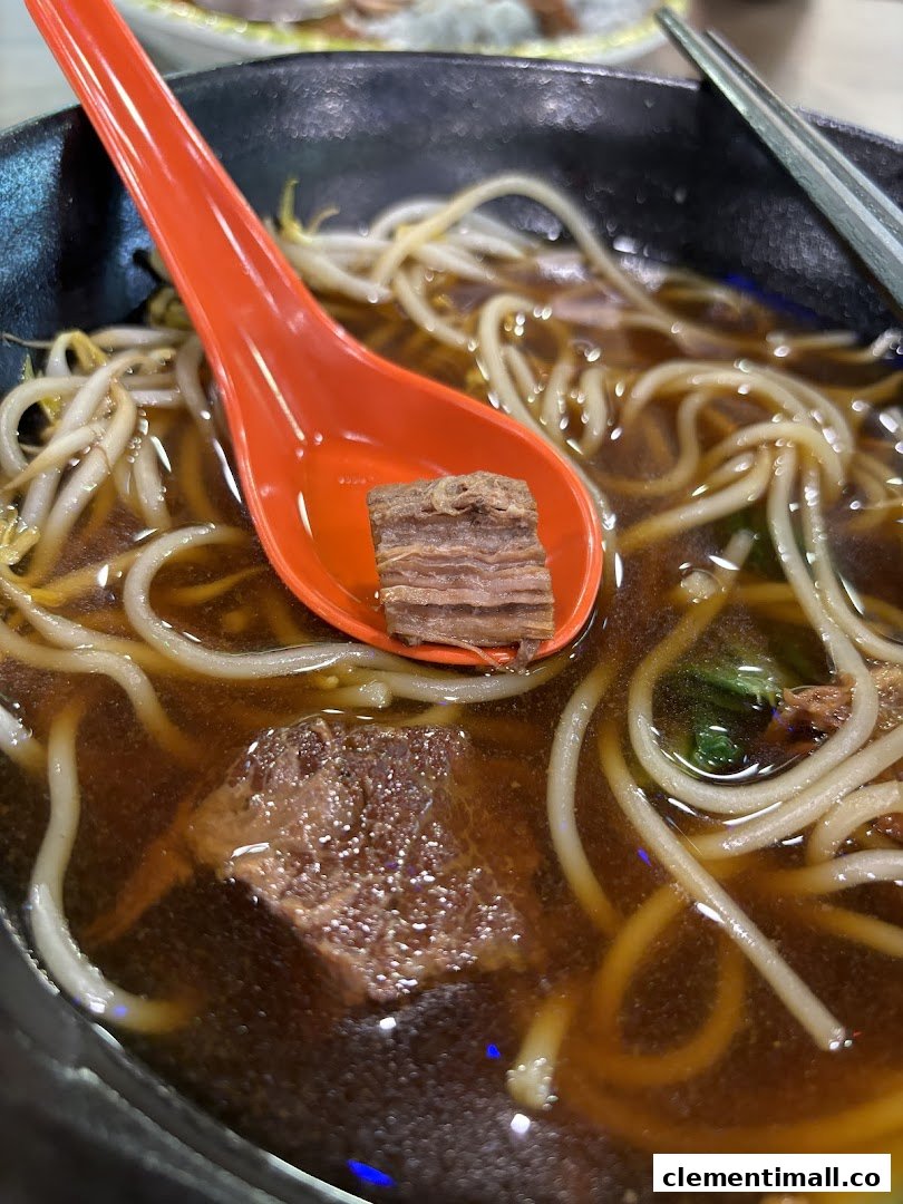A close-up of a hearty bowl of beef noodles with bean sprouts, featuring a tender beef chunk on a spoon.
