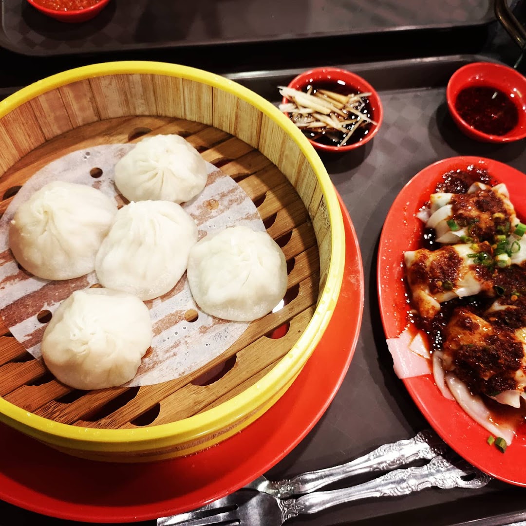 A close-up of delicious steamed dumplings in a bamboo basket and chili wontons on a red plate.