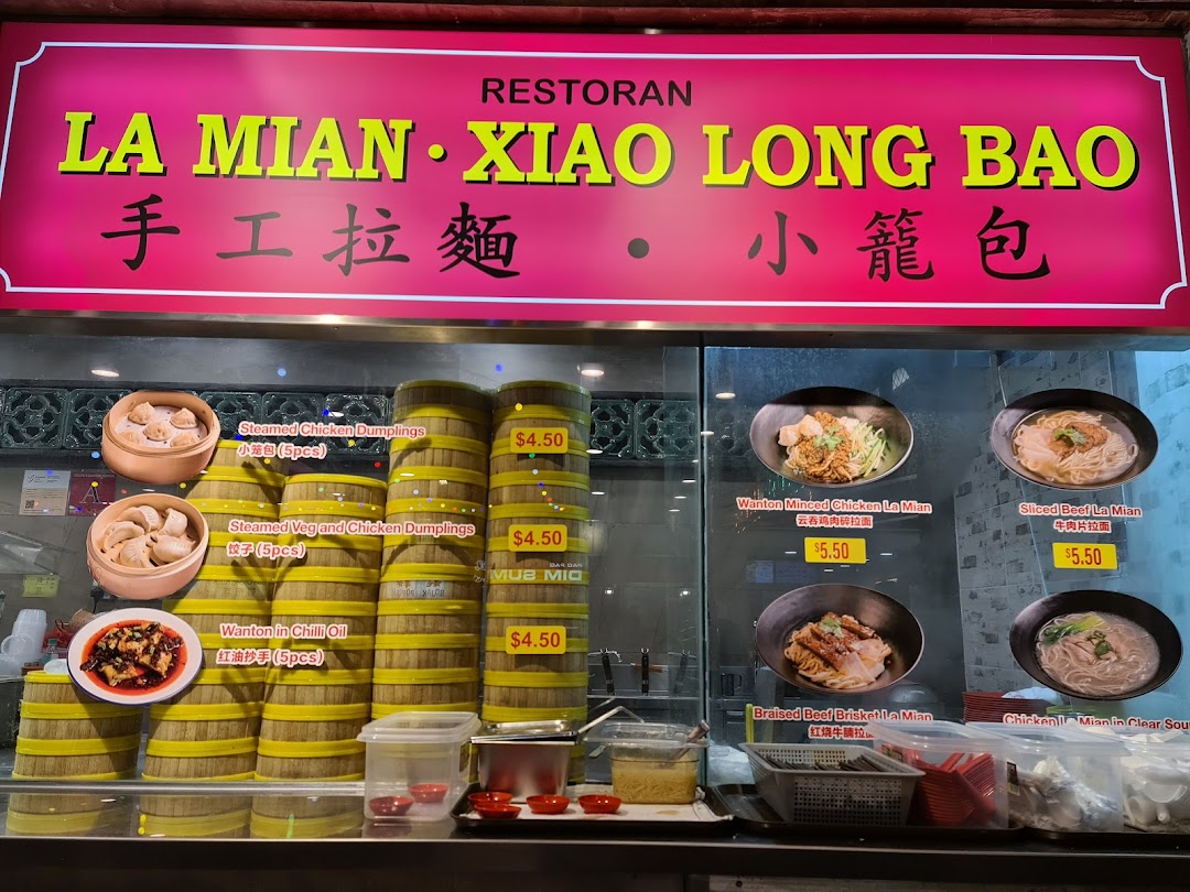 A vibrant display of authentic Chinese dumplings and La Mian noodles with prices at a food stall counter.
