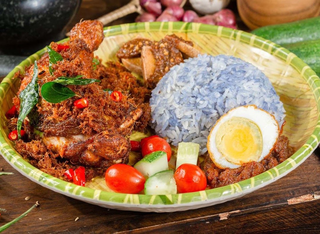 A vibrant plate of Nasi Lemak featuring crispy fried chicken, blue pea rice, and a fried egg.