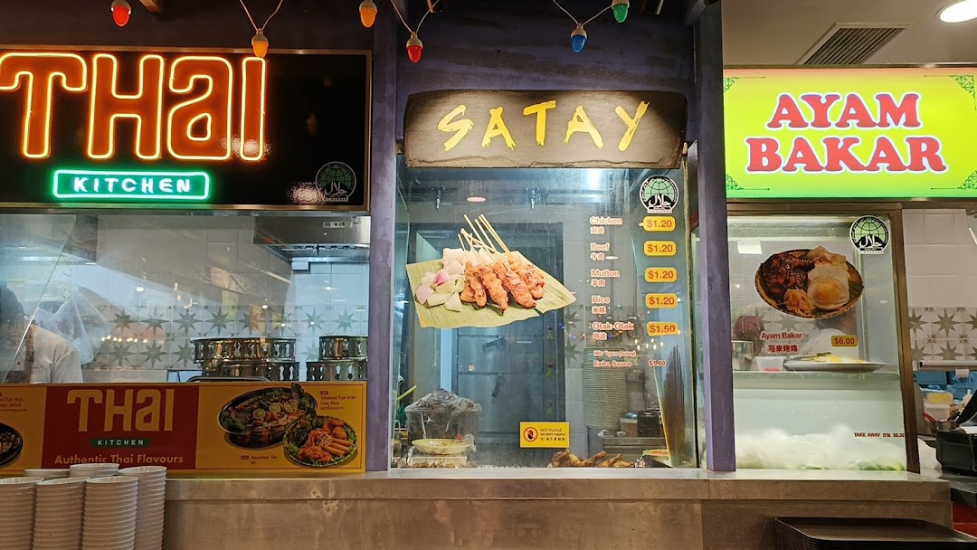 A vibrant food stall offering Thai cuisine, satay skewers, and Ayam Bakar with visible prices.