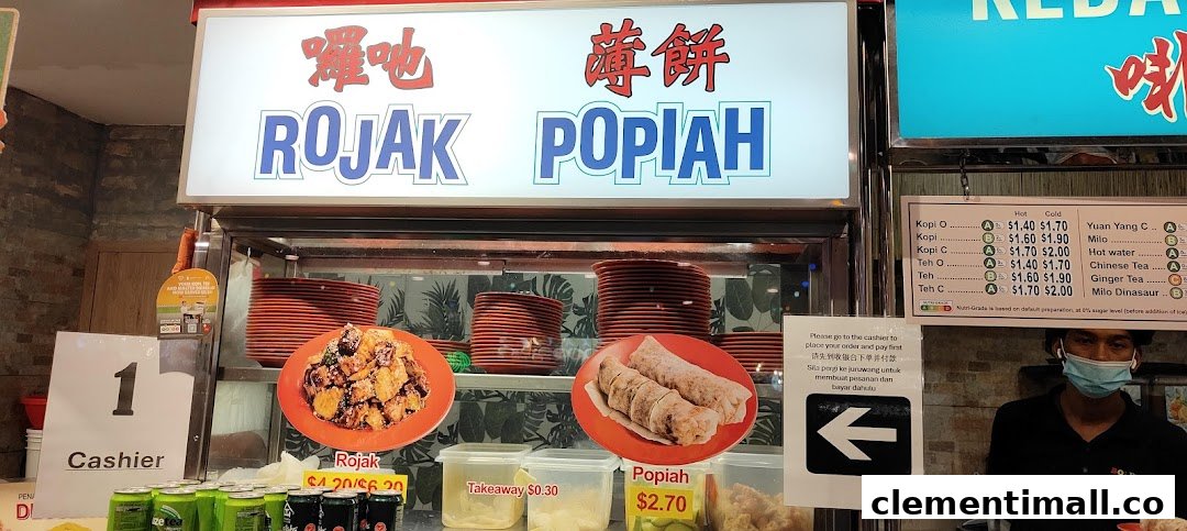 A food stall counter featuring signage for Rojak and Popiah, with a drinks menu and a staff member.