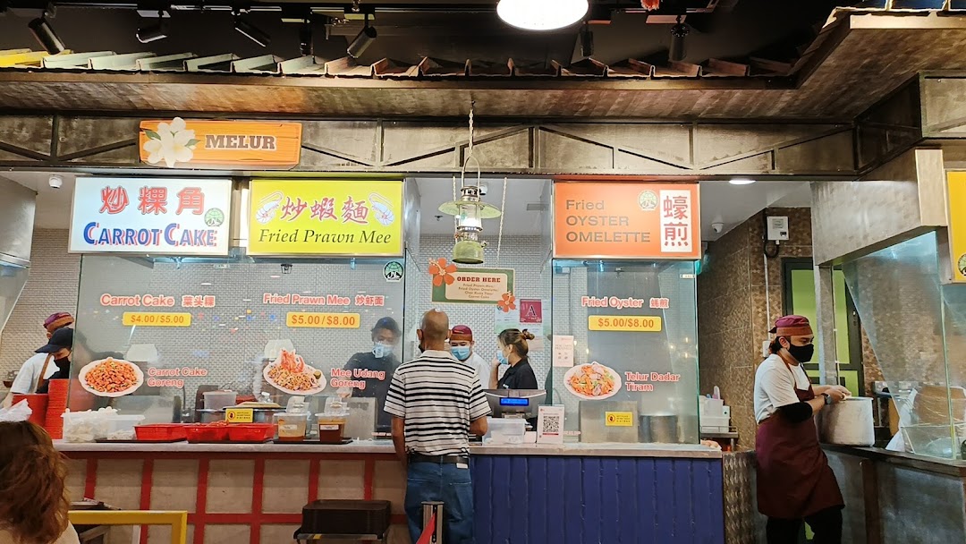 A bustling food stall counter at Melur, serving local dishes like Carrot Cake and Fried Prawn Mee.