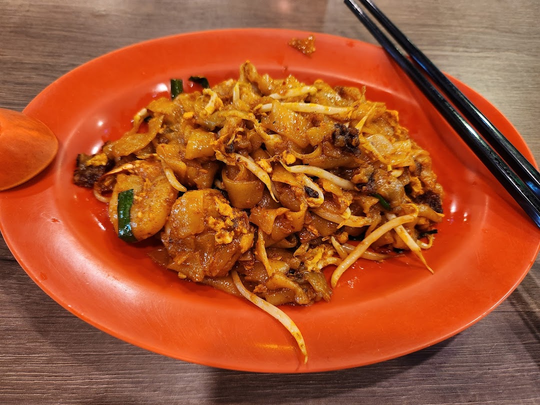 A vibrant plate of Char Kway Teow with prawns and bean sprouts on an orange plate.