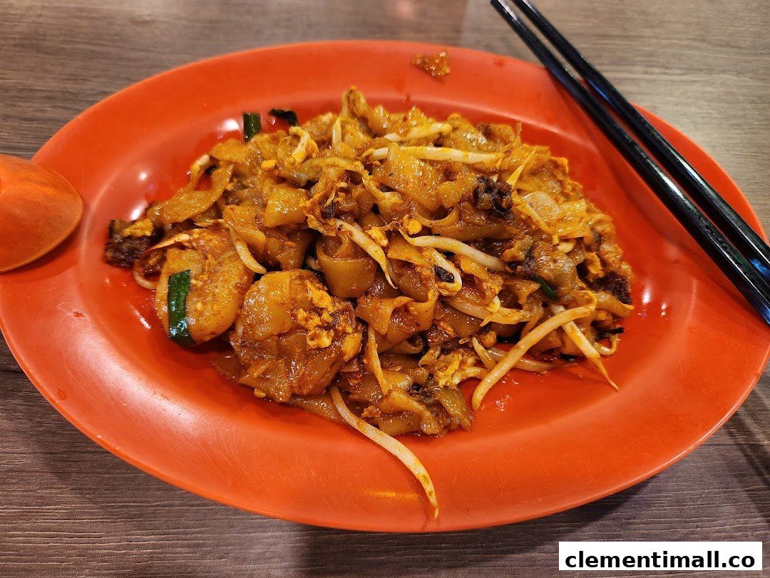 A vibrant plate of Char Kway Teow with prawns and bean sprouts on an orange plate.