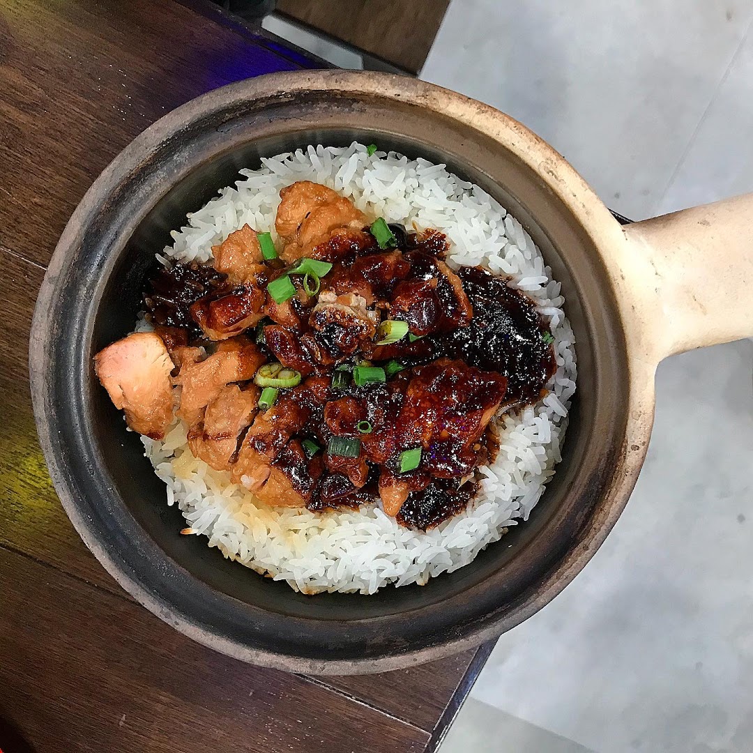 A close-up of a delicious claypot chicken rice dish, garnished with spring onions.
